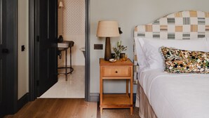 A bedroom with a bed, a nightstand, a lamp, and a bathroom visible through an open door. - Luxury Stay in Heart of the Cotswolds (Cheltenham)