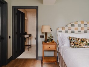 Ein Schlafzimmer mit Bett, Nachttisch, Lampe und einem durchgegangenen Tür erkennbaren Badezimmer.