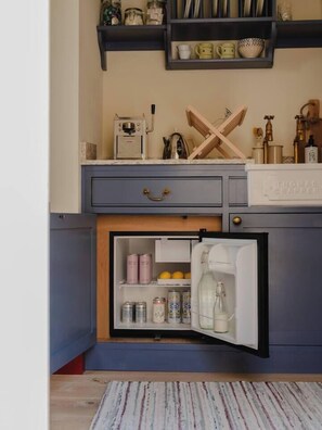 A kitchen with a built-in refrigerator, shelves with jars and bottles, and a coffee machine.