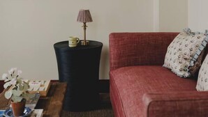 A living room with a red sofa, a framed map on the wall, a side table with a lamp, and a small potted plant.