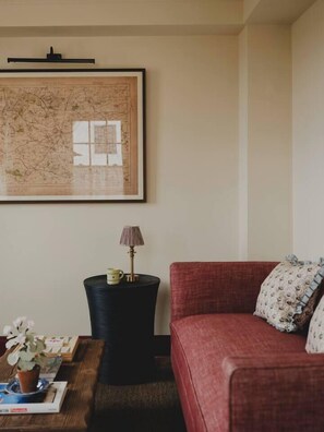 A living room with a red sofa, a framed map on the wall, a side table with a lamp, and a small potted plant.