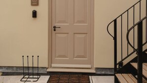 A beige door with a doorknob and a mail slot, a small wall-mounted light, and a plaque above the door.