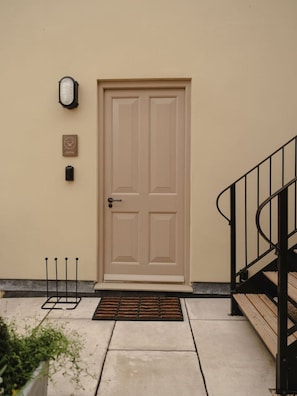 A beige door with a doorknob and a mail slot, a small wall-mounted light, and a plaque above the door.