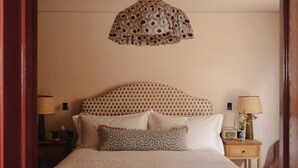 A neatly made bed with a patterned headboard, a bedside table with a lamp, and a hanging light fixture.