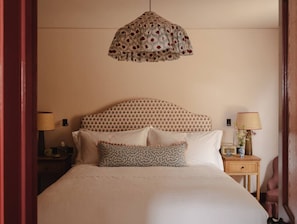 A neatly made bed with a patterned headboard, a bedside table with a lamp, and a hanging light fixture.
