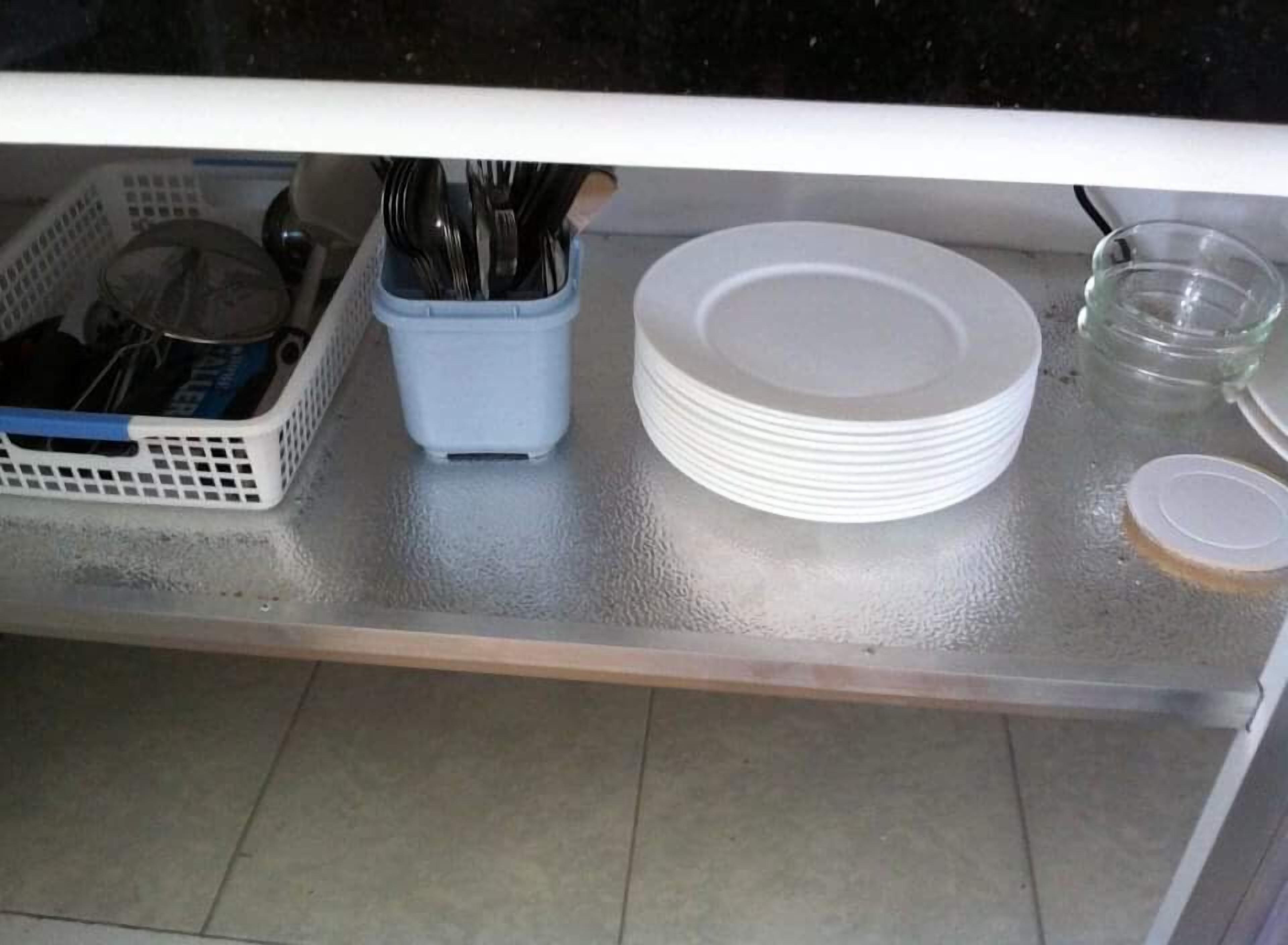 A kitchen counter with a dish rack, a container holding utensils, stacked plates, and a glass jar.