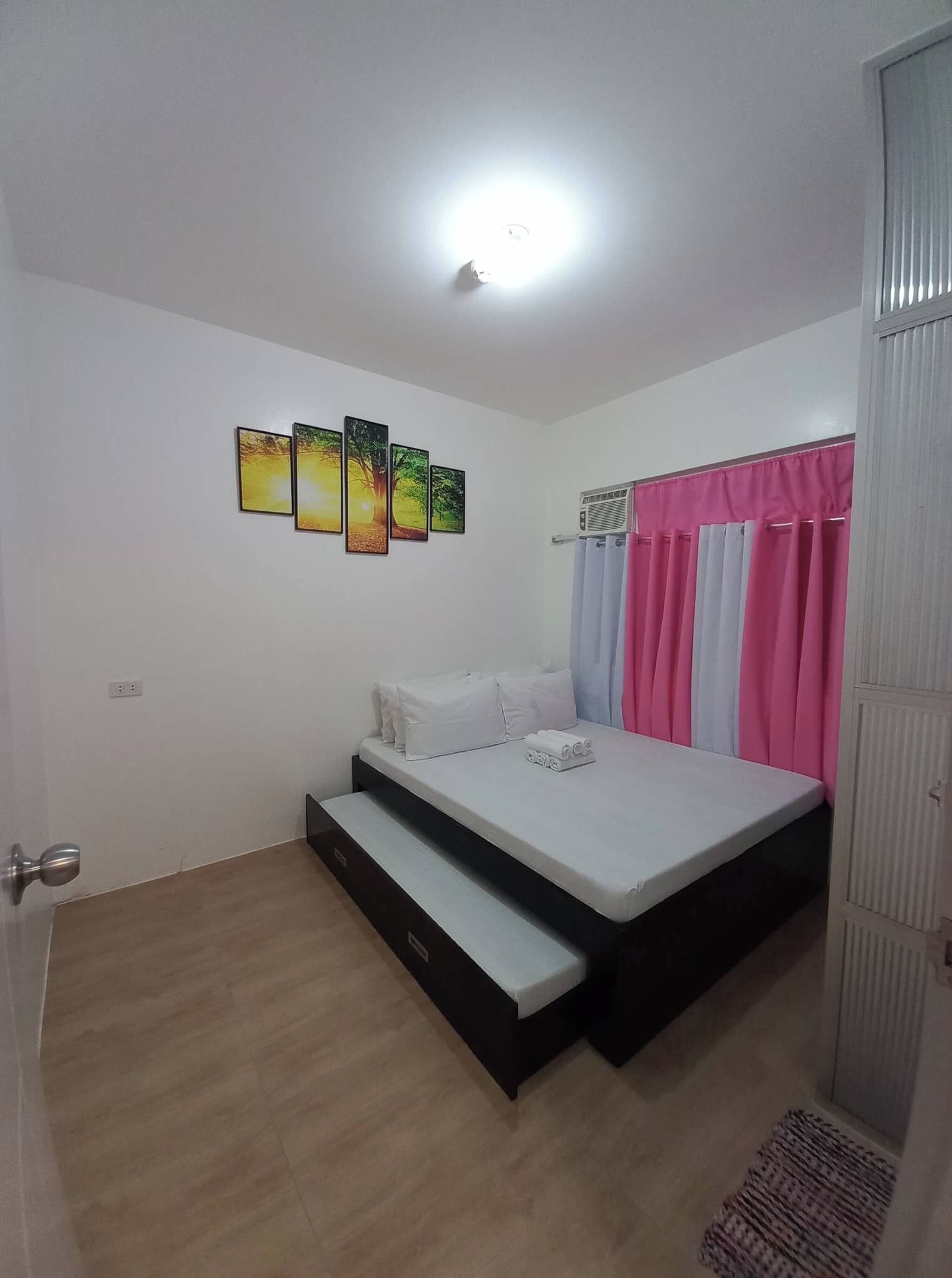 A bedroom with a bed, a small bench, a wall-mounted air conditioner, and a set of curtains.