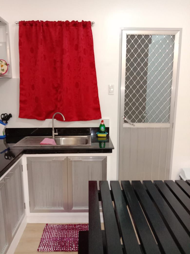 A compact kitchen with a sink, a red curtain, and a window with a metal screen.