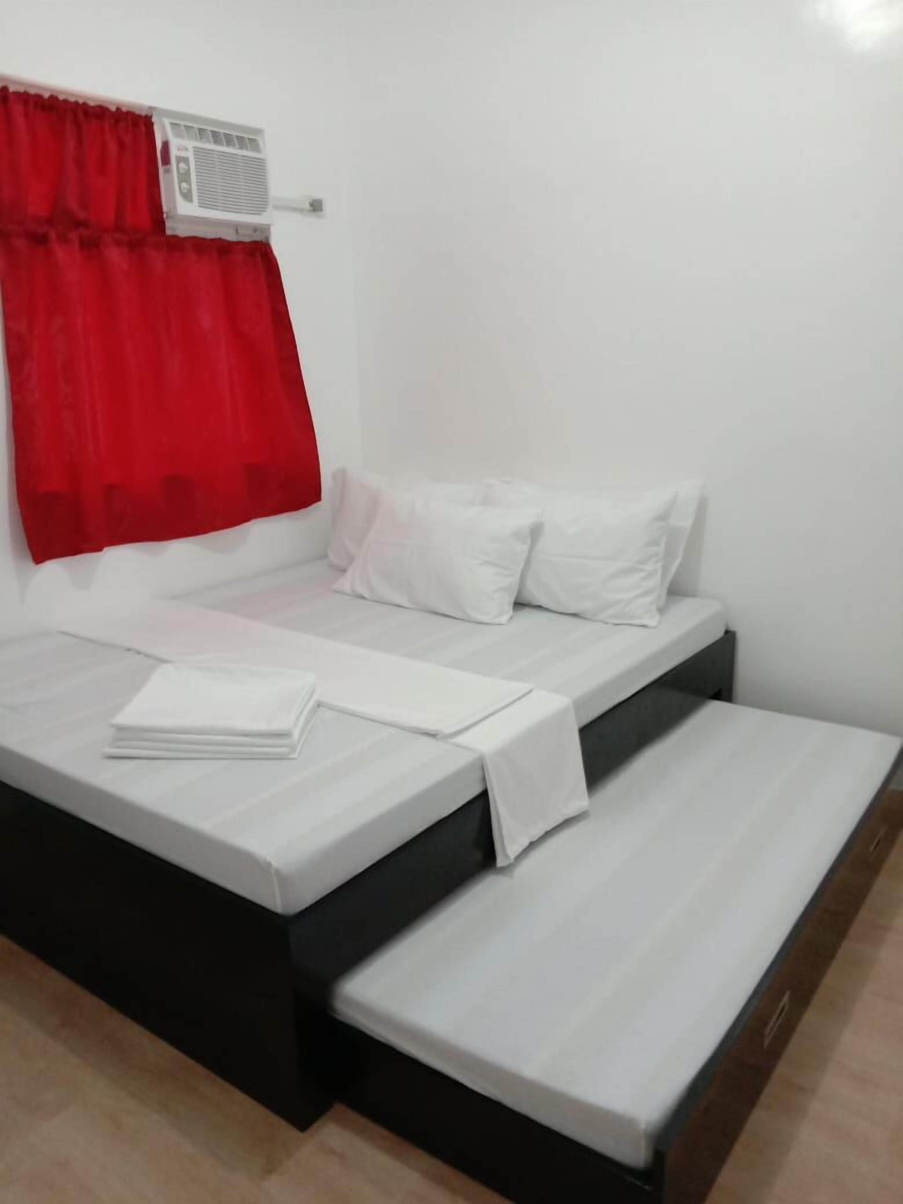 A single bed with white bedding, a red curtain, and a wall-mounted air conditioner.