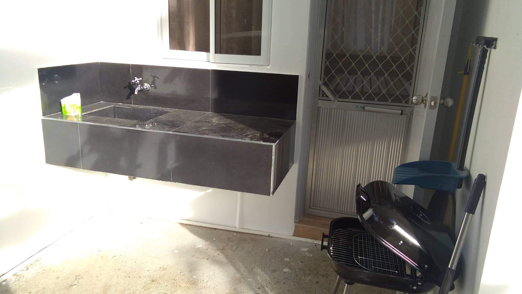 A kitchen with a black countertop, a stainless steel sink, and a grill.