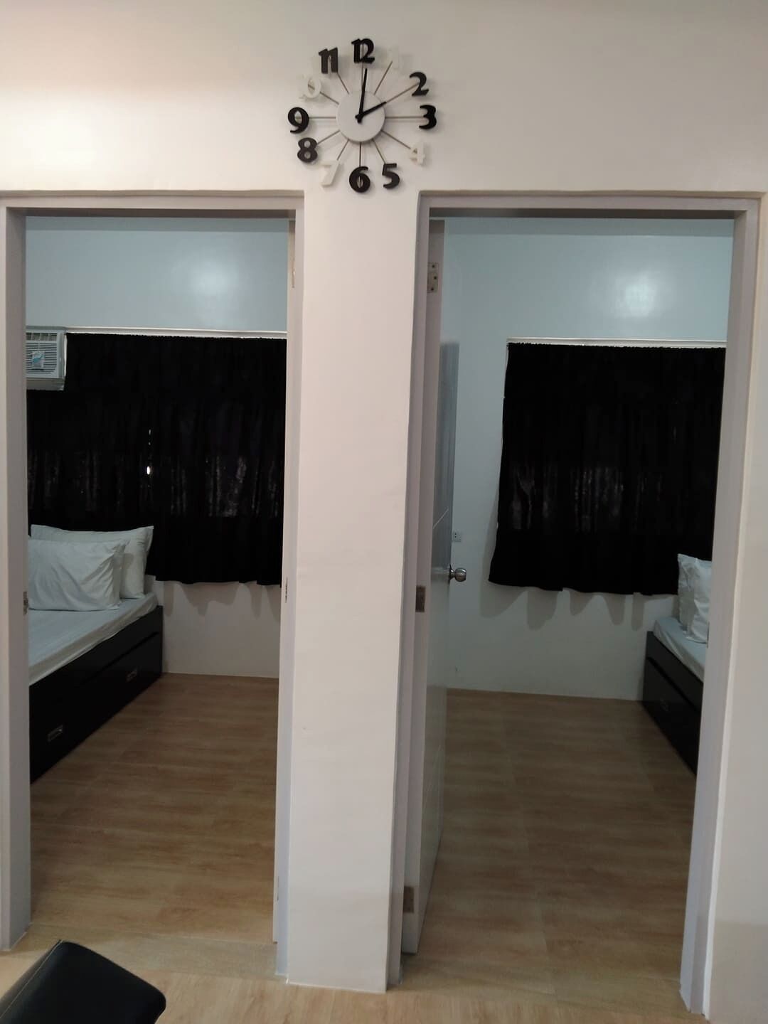 A room with two beds, a wall clock, and a door leading to another room.