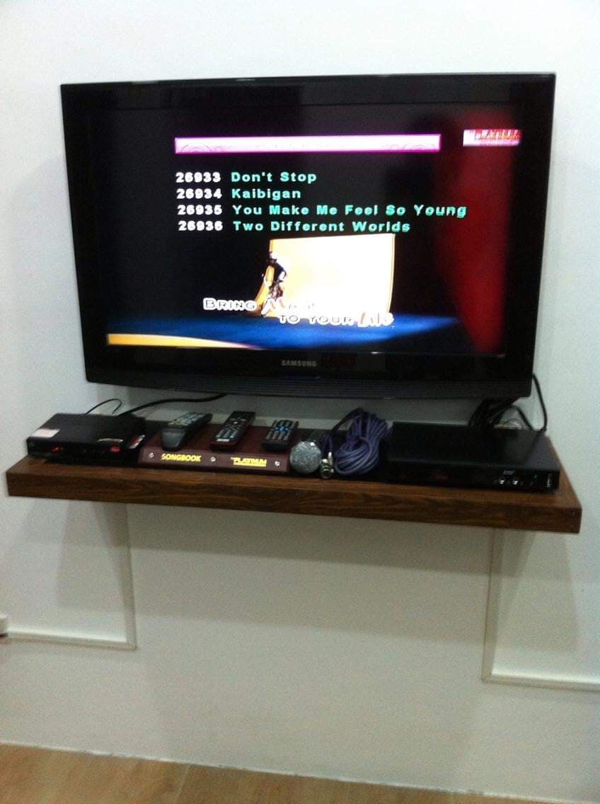 A television on a wooden shelf displaying a music video with song titles.