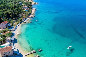 Eine Luftaufnahme einer Küstenregion mit klarem, türkisblauem Wasser, einem Sandstrand und einer Reihe von Gebäuden entlang der Uferlinie.