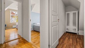 A hallway with wooden flooring, white doors, and a view into a bedroom with a bed and a window. - Bergen Villa - Charming 3 Bedroom a View (Bergen)