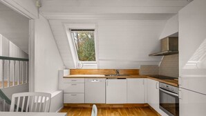 A compact kitchen with white cabinetry, a wooden countertop, a built-in oven, and a window with a view of trees. - Bergen Villa - Charming 3 Bedroom a View (Bergen)