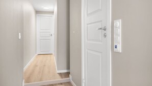 A hallway with a wooden floor, white walls, and a white door with a lock and a control panel on the wall. - Dream Apartment – Central Living at Its Best! (Bergen)