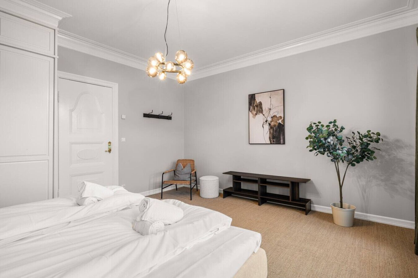 A bedroom with a bed, a chair, a bench, a plant, and a wall-mounted artwork.