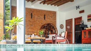 A poolside area with a brick wall, wooden furniture, and a refrigerator. - 3BR Boutique Villa, Private Pool (Krong Siem Reap)