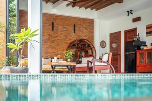Un área junto a la piscina con pared de ladrillo, muebles de madera y un refrigerador.