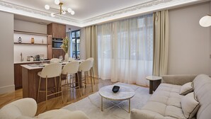 Un salon moderne avec un canapé, une table basse et un coin repas comprenant des chaises, et une cuisine en arrière-plan.