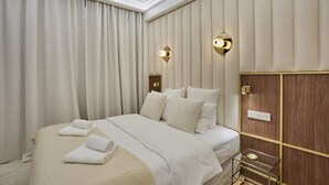Une chambre d’hôtel avec un grand lit, des rideaux beiges, deux appliques murales et un mur recouvert de panneaux en bois.