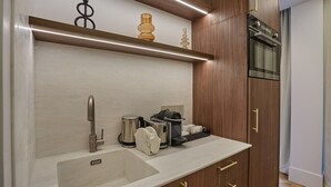 Une cuisine moderne dotée d’un évier encastré, d’appareils électroménagers en acier inoxydable, de meubles de rangement en bois et d’un plan de travail sur lequel se trouvent une machine à café et des tasses.