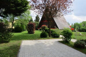 Ein Weg führt zu einem Gebäude mit einem dreieckigen Dach und roten Akzenten, umgeben von gepflegter Bepflanzung und blauem Himmel.