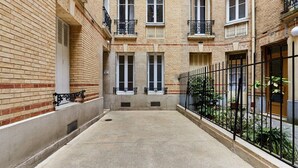 A courtyard with a brick building, a concrete floor, and a metal fence. - Charming 1 bedroom apartment Eiffel Tower (Paris)
