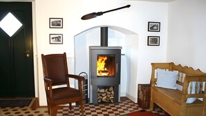 Ett rum med en vedeldad kamin, ett rutmönstrat golv, en trästol, en soffa och inramade tavlor på väggen.