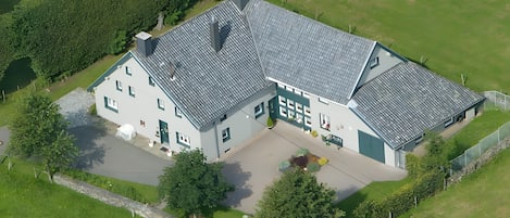 Eine Luftaufnahme eines großen, zweistöckigen Hauses mit geneigtem Dach, einer Auffahrt und einem gepflegten Rasen.