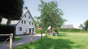 Ett vitt hus med ett sluttande tak, en asfalterad uppfart och en gräsyta med en bänk.