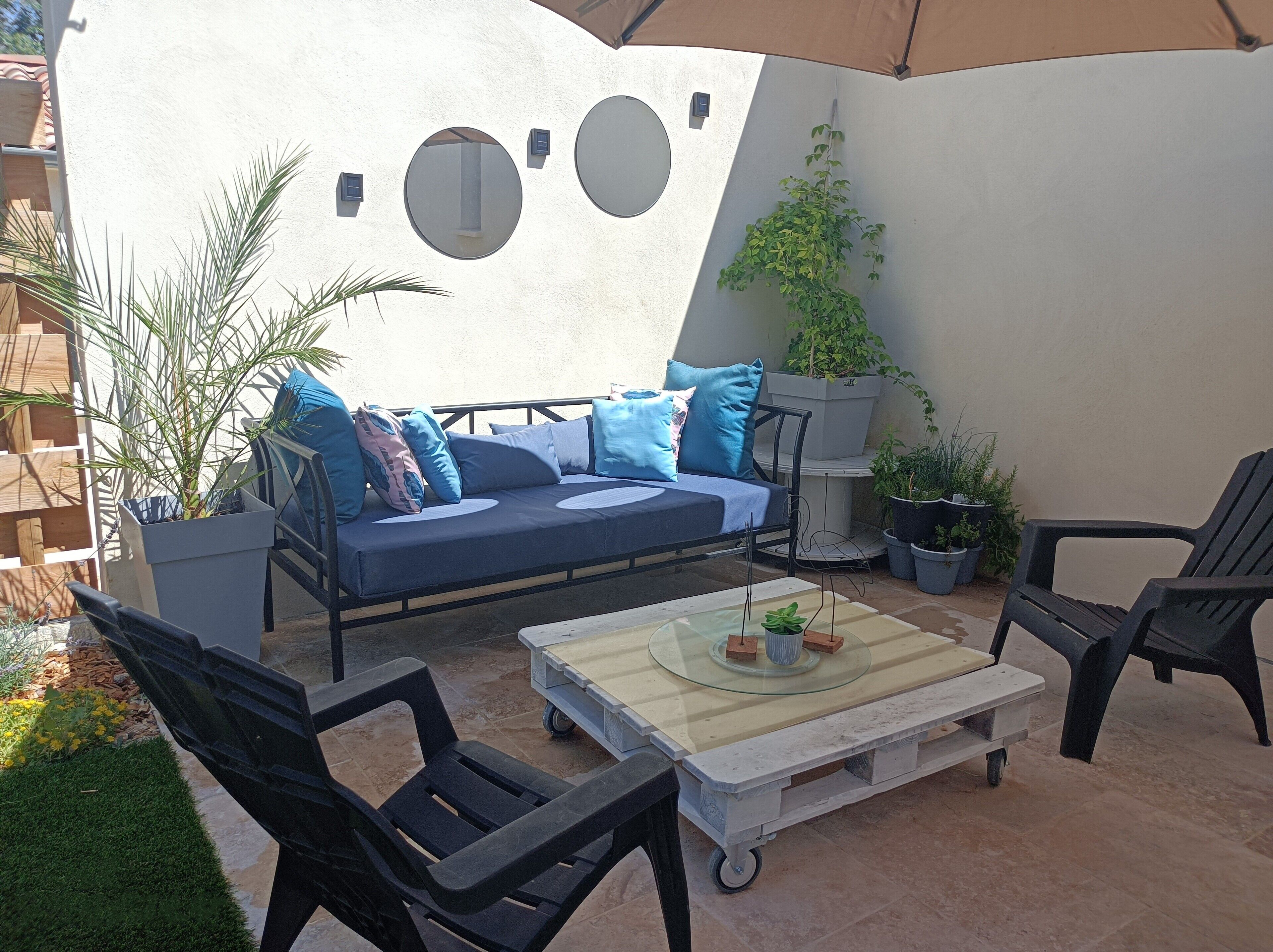 A patio area with a blue sofa, black chairs, a glass table, and potted plants.