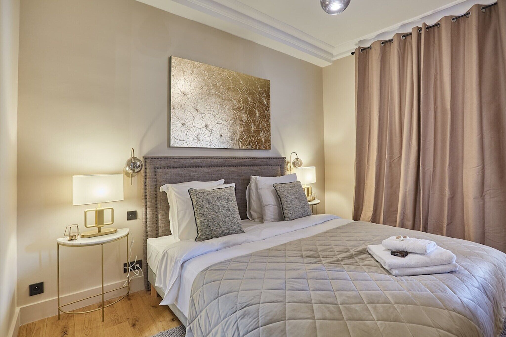 A neatly arranged bedroom with a large bed, two bedside lamps, a wall-mounted artwork, and a window with curtains.