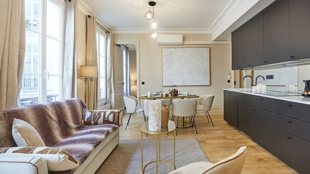 Ein modernes Wohnzimmer mit einer Couch, einem Esstisch, Stühlen und einer Küche mit dunklen Schränken und einer Marmorarbeitsplatte.