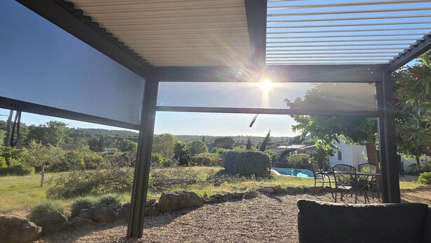 Un'area esterna coperta con vista su una piscina e del verde.