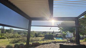 A covered outdoor area with a view of a pool and greenery.