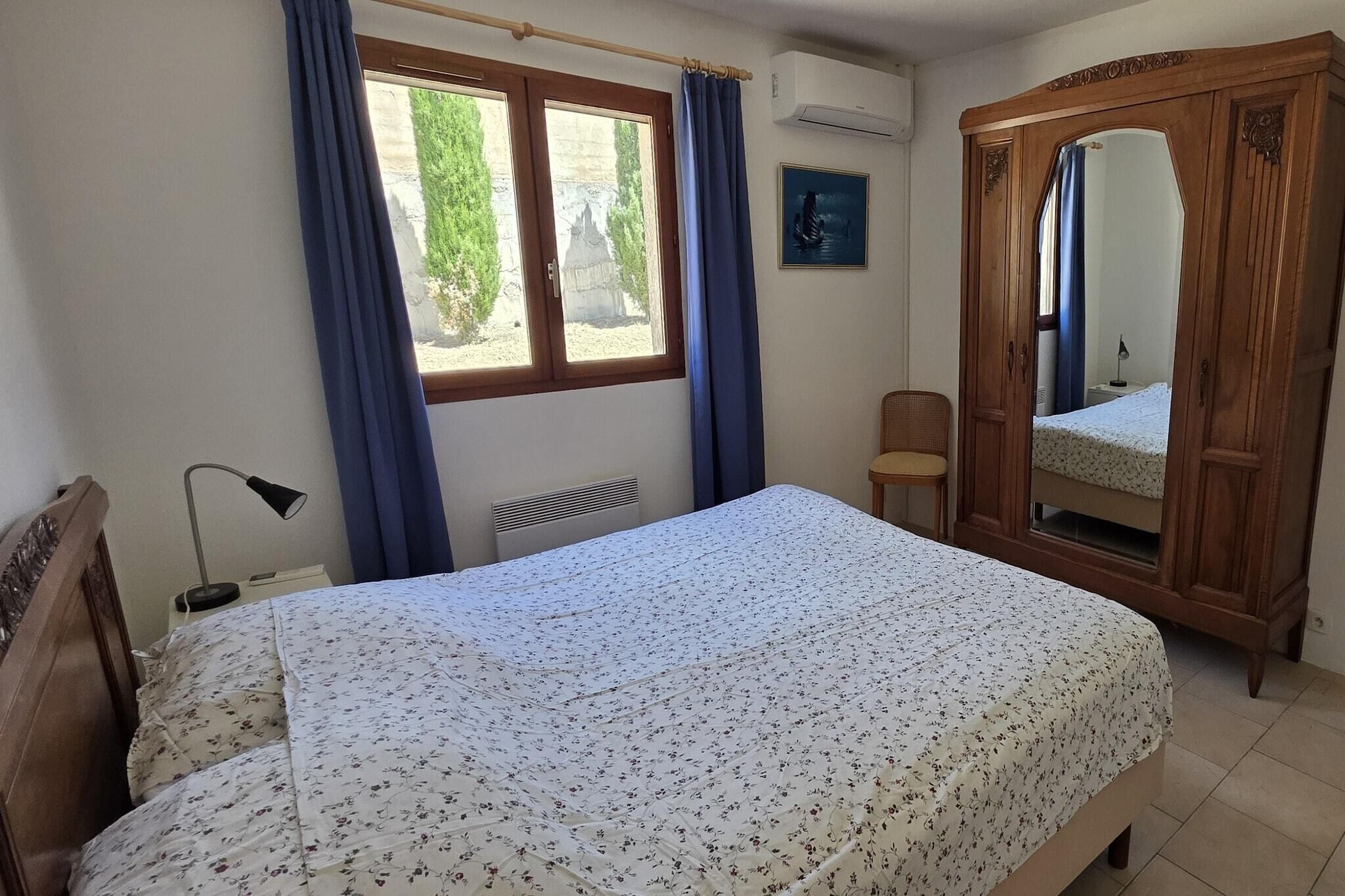 Un dormitorio con cama, armario de madera, ventana con cortinas, una silla y mesita de noche.