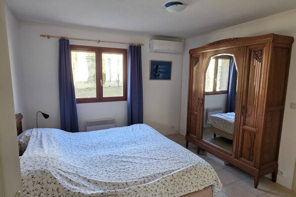 Un dormitorio con cama, armario, ventana con cortinas, equipo de aire acondicionado y radiador.