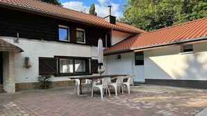 En terrasse med et bord og stole, et træhegn og en bygning med rødt tegltag.