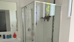 Ett modernt badrum med en dusch som är avskärmad med glasväggar, en vit toalett och ett handfat med plats för toalettartiklar.