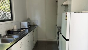 Ett kök med vita skåp, en diskho i rostfritt stål, en mikrovågsugn och ett kylskåp.