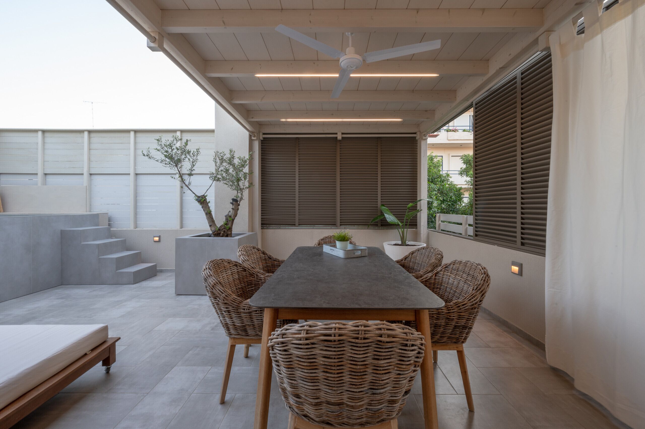 A modern patio with a dining table, wicker chairs, a ceiling fan, and potted plants.