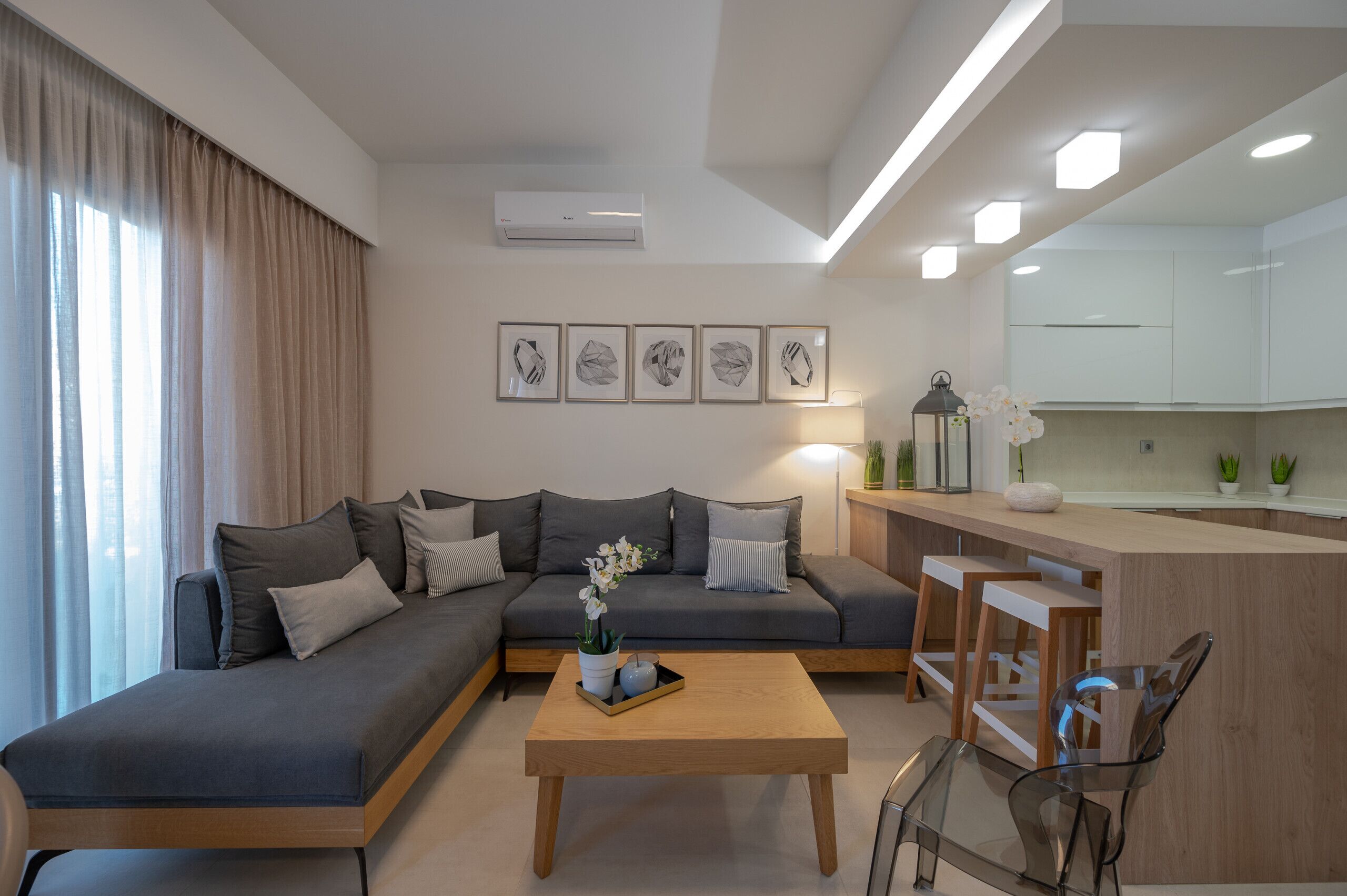 A modern living room with a grey sofa, a wooden coffee table, and a kitchen area with white cabinets.