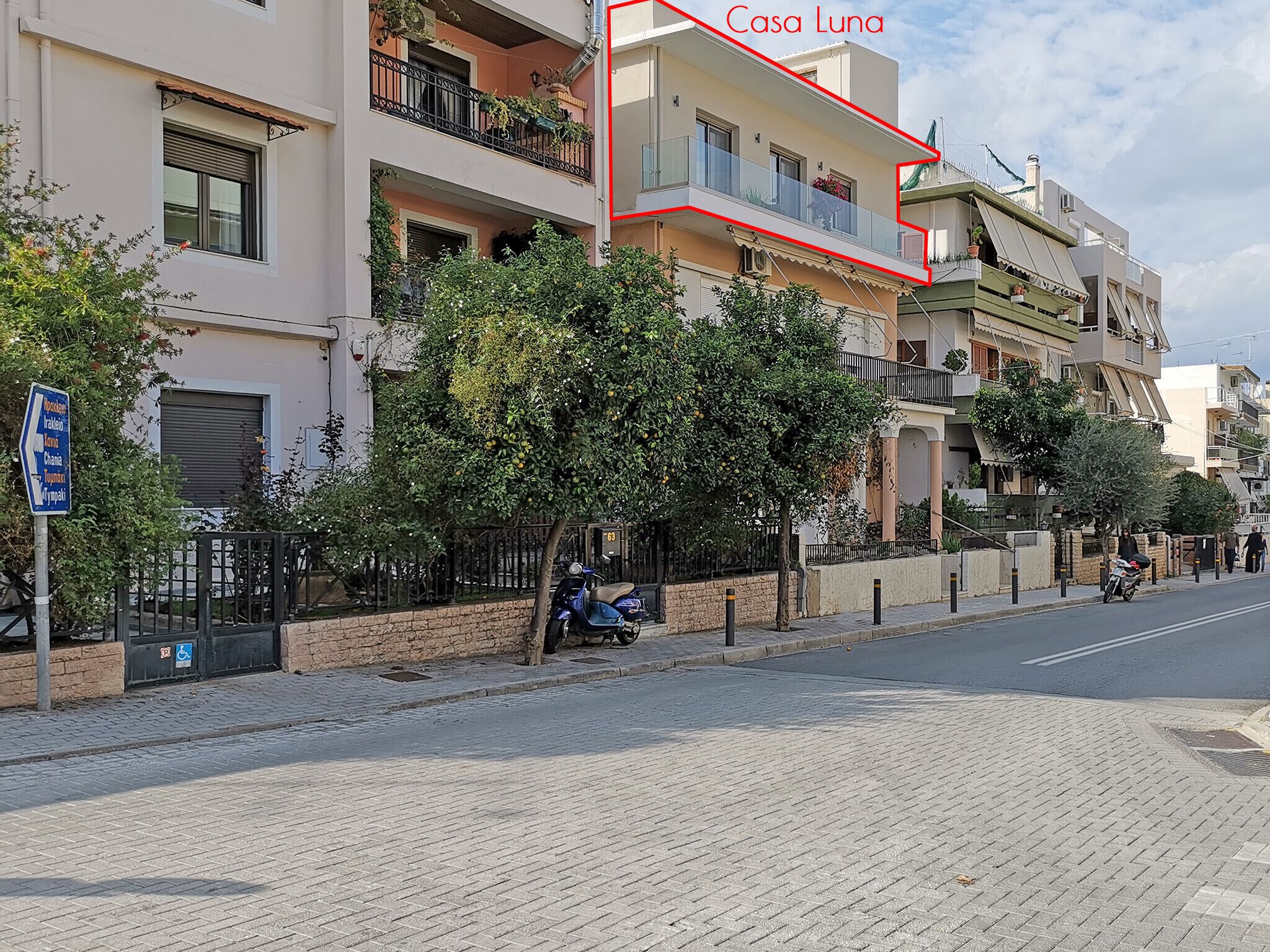 Un edificio de varios pisos con balcones, una acera empedrada y una calle.
