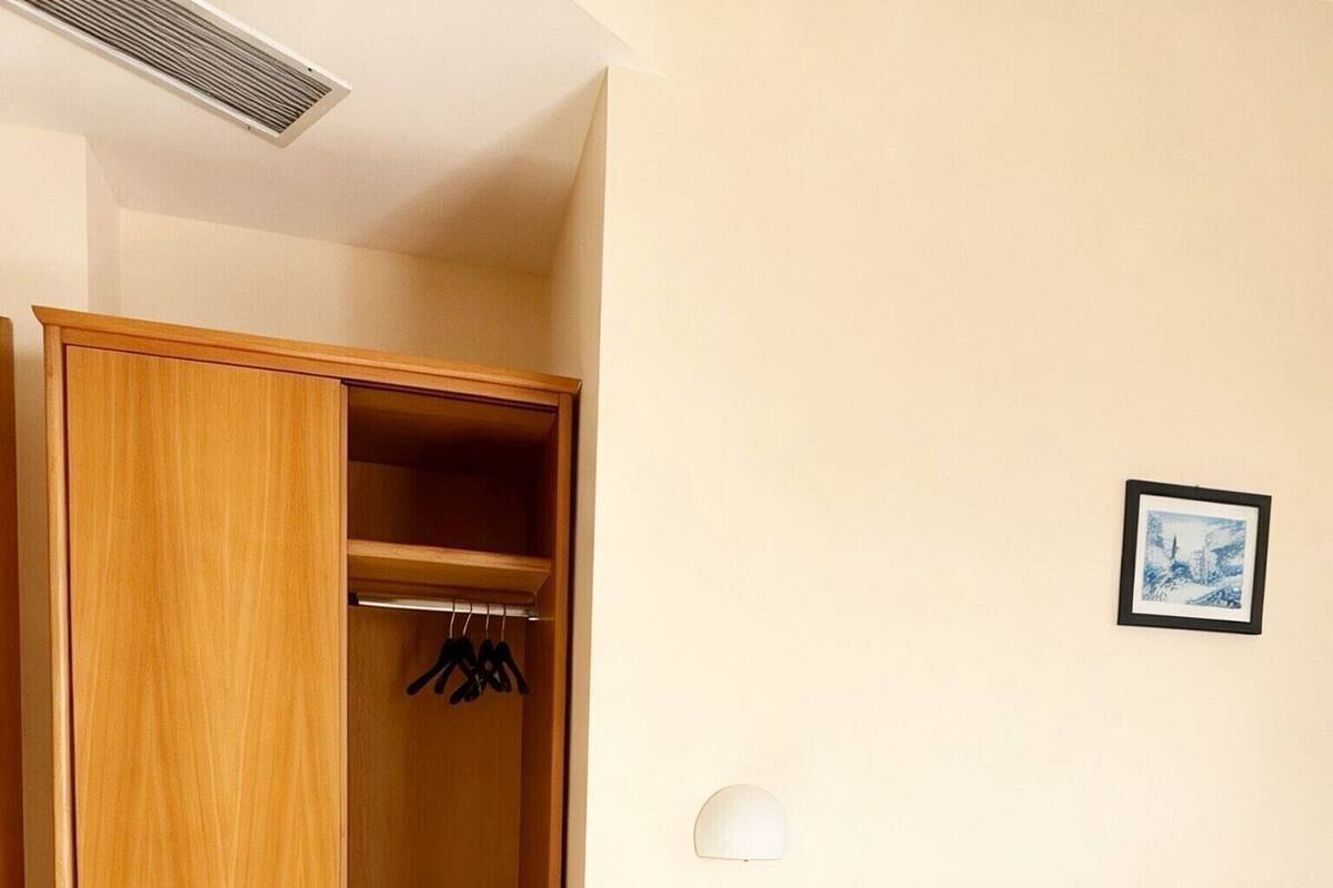 Une chambre d’hôtel avec une armoire en bois, une table de chevet avec une lampe et un lit avec du linge de lit blanc.
