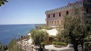 Un hotel frente al mar, con zona de estar al aire libre cubierta y un edificio tradicional con balcones.