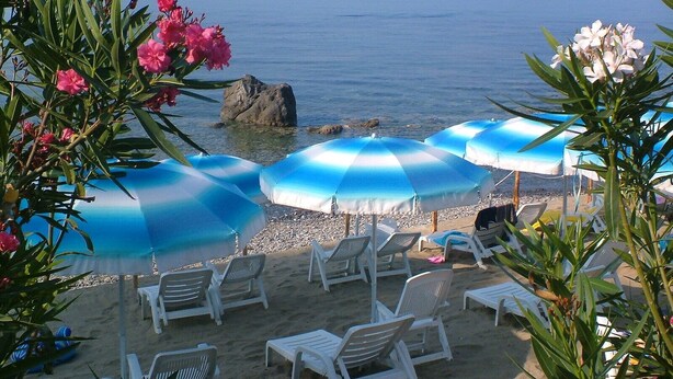 Una playa con sillones blancos y sombrillas azules, con vista al mar.