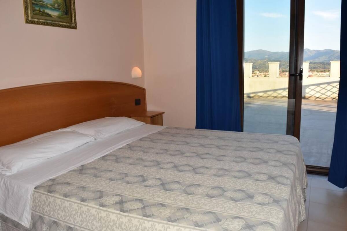 Une chambre à coucher comprenant un lit, une table de chevet, une lampe fixée au mur et une grande fenêtre donnant sur les montagnes.