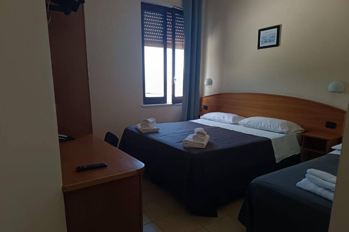 Une chambre d’hôtel avec deux lits, un bureau, une chaise et une fenêtre avec des stores.
