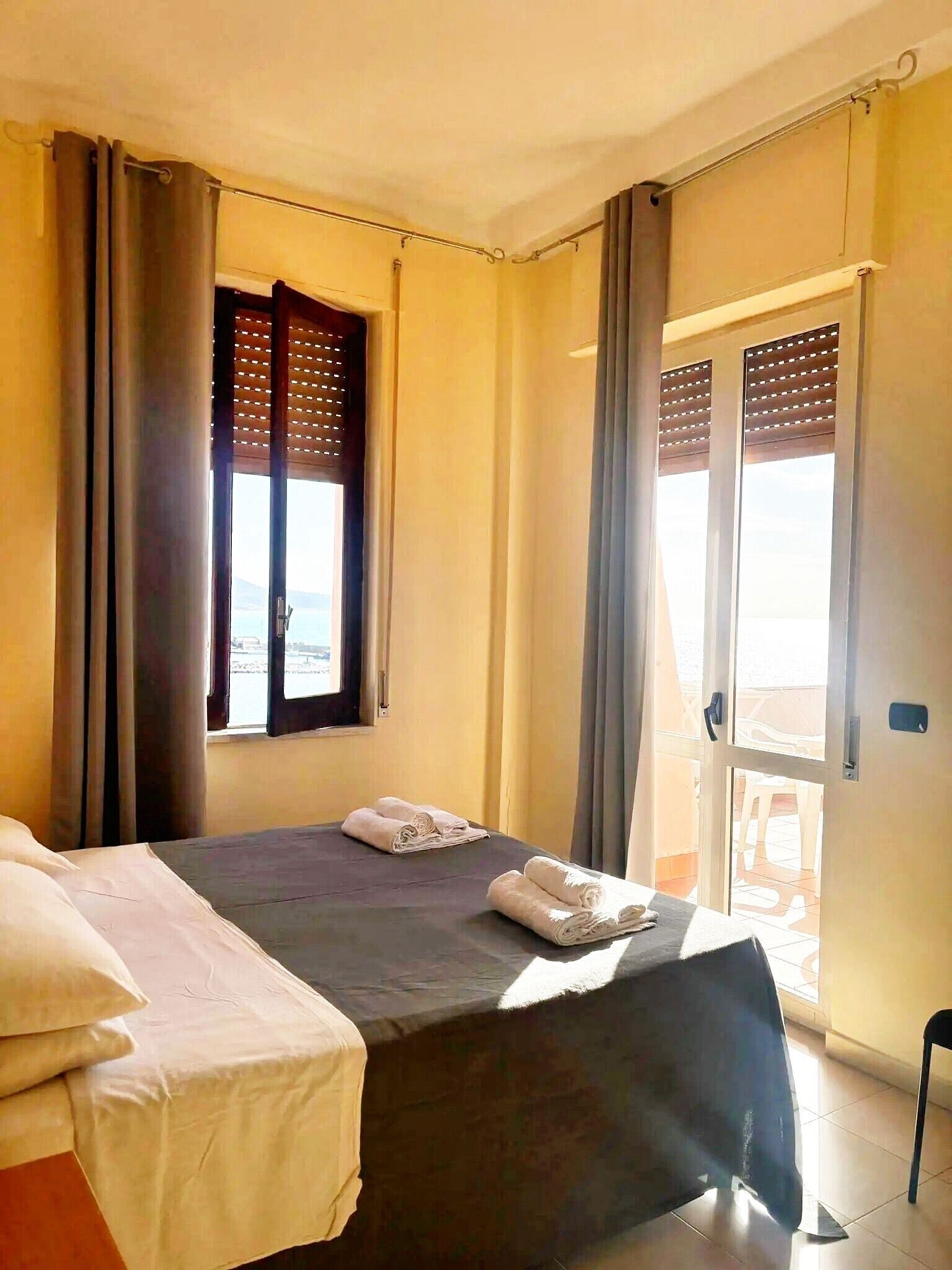 Ein Hotelzimmer mit Bett, Fenster mit Jalousien, einer Tür mit Blick und einem Balkon.